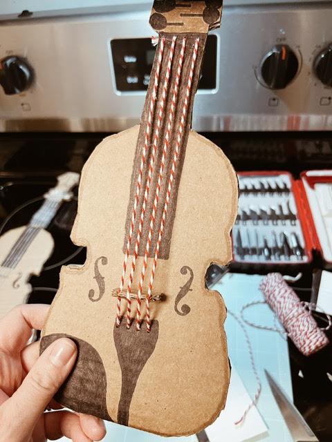 step 5 of diy cardboard viola is assembling the strings over the bridge